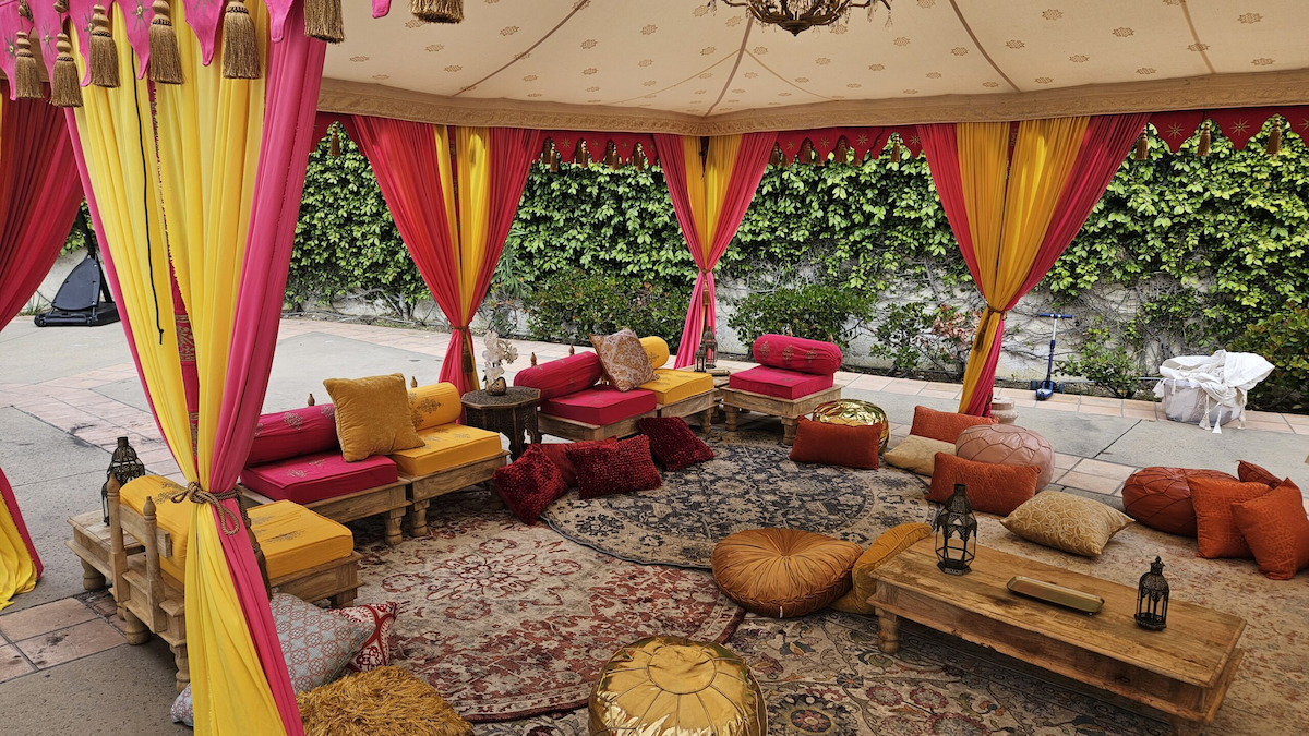 Luxury lounge seating with colorful velvet bolsters, gold poufs, and patterned rugs inside a wedding tent.