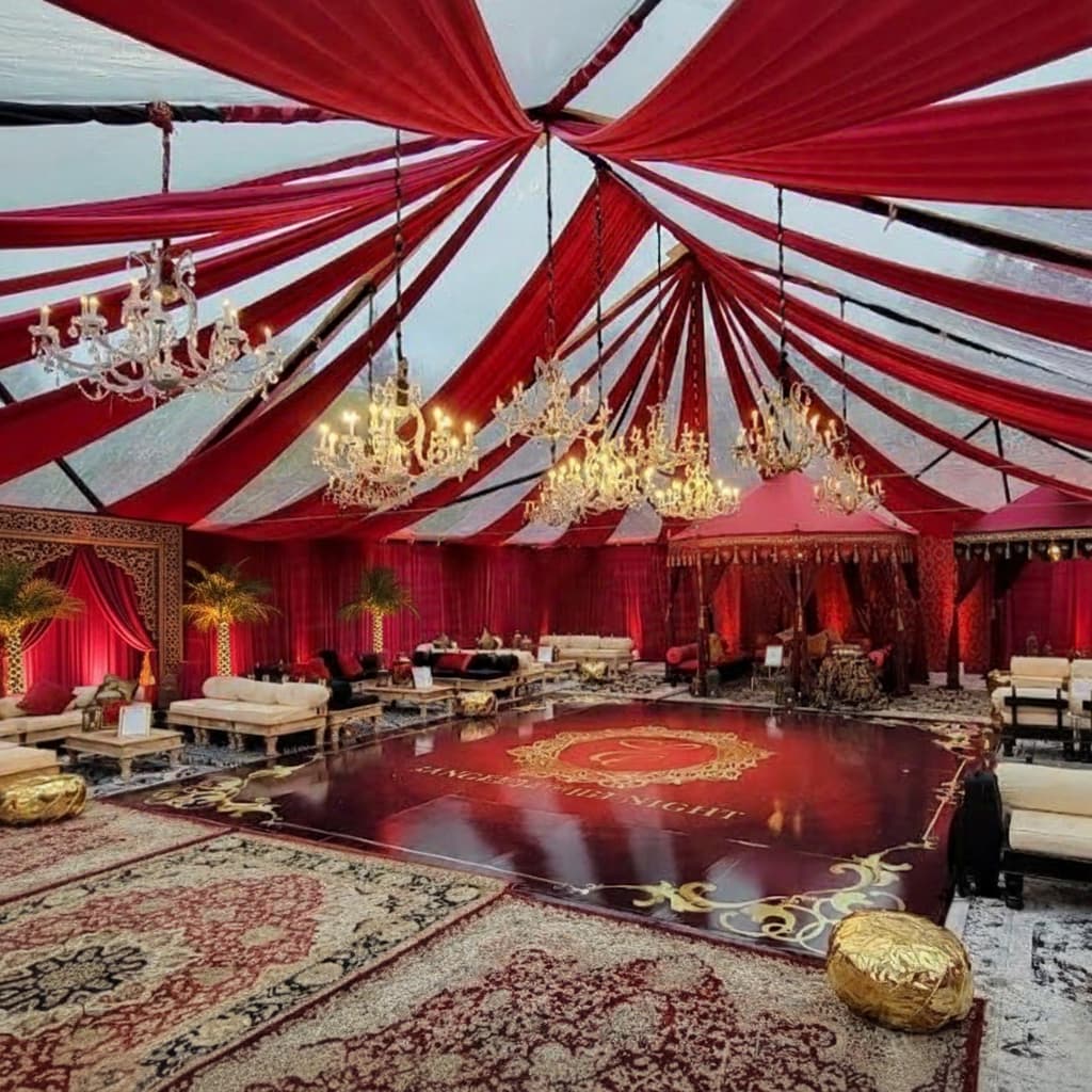 A grand Sangeet and Garba stage featuring a custom red dance floor, ornate chandeliers, red ceiling draping, and luxury lounge furniture for a California Indian wedding.