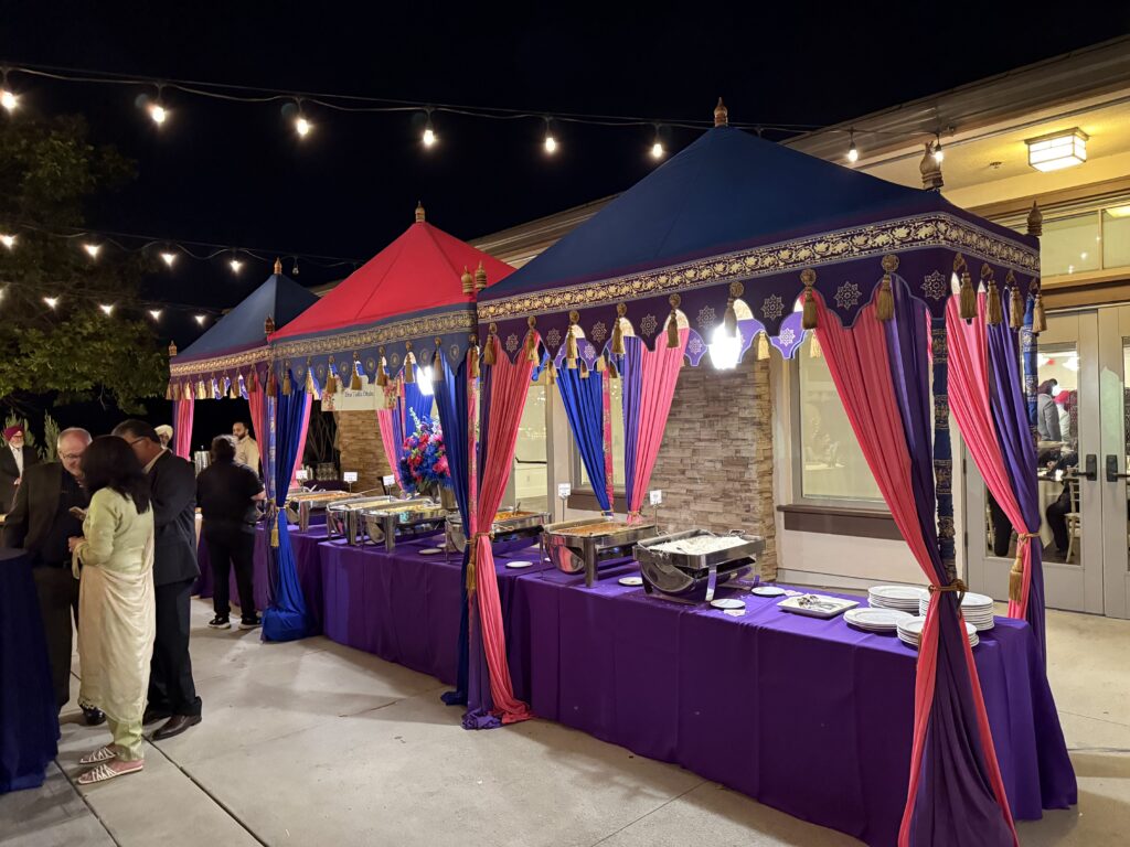 Mini Taj Tent buffet setup at night with string lights, purple linens, and colorful draping